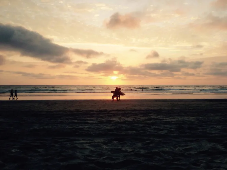 Silhouetten von Surfern am Strand vor dem Sonnenuntergang unter Wolken