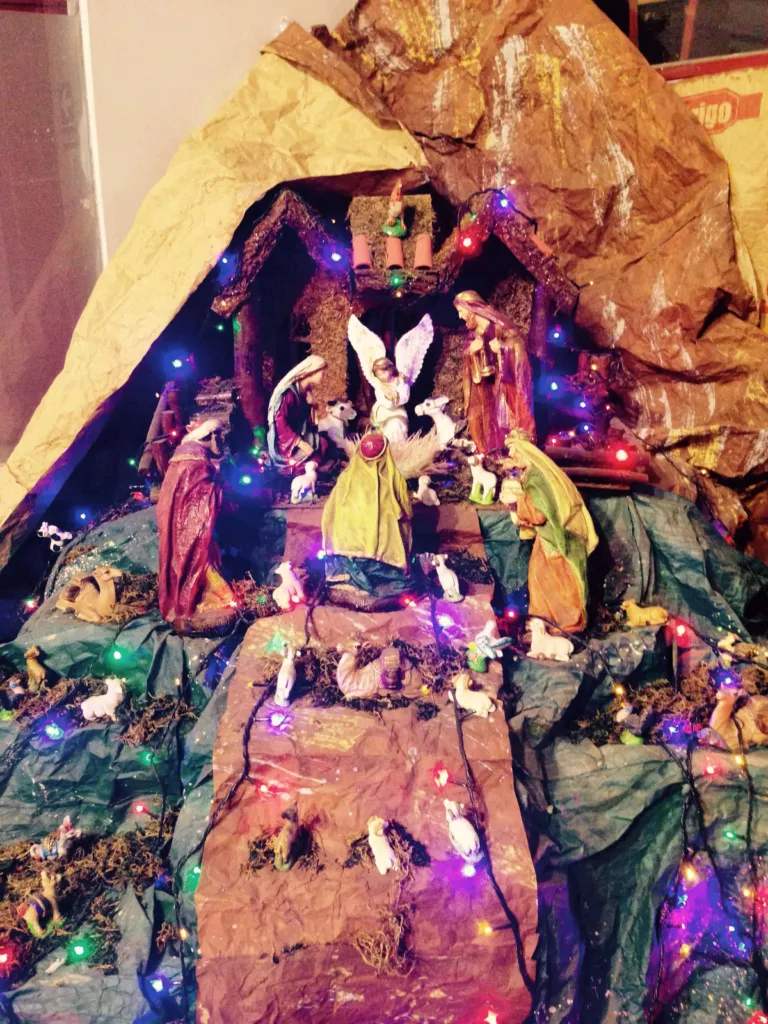 Beleuchtete Weihnachtskrippe mit Engel und Figuren zwischen Papierfelsen und Lichterketten