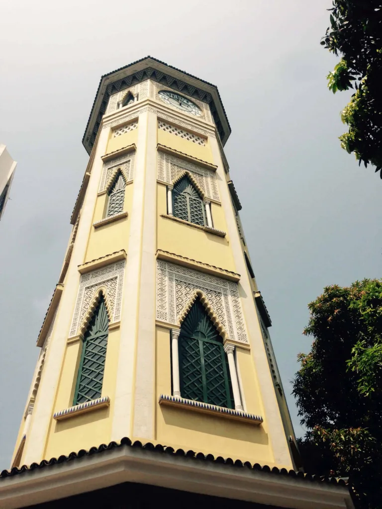 Hoher gelber Turm mit grünen Fensterläden, von unten fotografiert