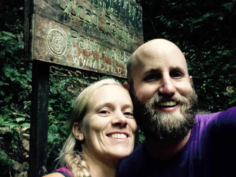 Ein lächelnder bärtiger Mann und eine blonde Frau machen ein Selfie vor einem Holzschild im Wald