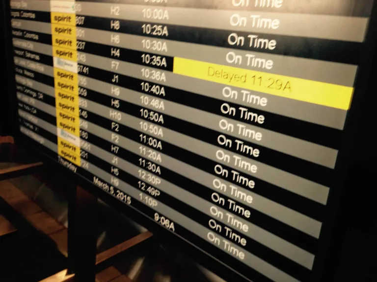 Schwarze Anzeigetafel im Flughafen mit vielen Zeilen On Time und einem gelb markierten Delayed