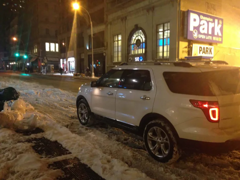 Weisser Geländewagen steht nachts in einer verschneiten Strasse in New York vor einem Parkhaus-Schild